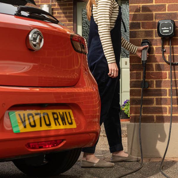 Vauxhall e-Corsa and Wallbox home charge unit, headless woman with hand on cable